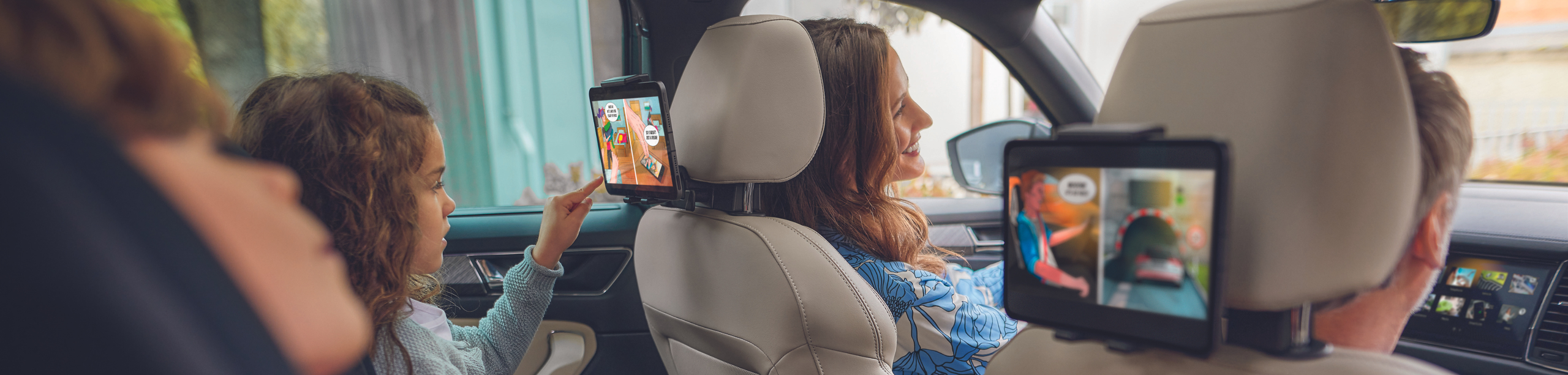 Familie sitzt im Auto und Kinder schauen auf Tablets